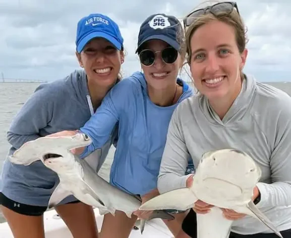 Three ladies hold two sharks with Island Lure Charters.